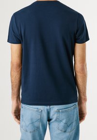 T-shirt in cotone blu navy con maniche corte, scollo rotondo, texture liscia, retro visibile, abbinato a jeans in denim azzurro chiaro con tasche.