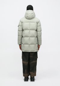 Φουσκωτό μπουφάν σε ανοιχτό γκρι με κουκούλα, με καπιτονέ τμήματα. Συνδυασμένο με σκούρες cargo παντελόνες με ξεθωριασμένο σχέδιο και μαύρα παπούτσια.