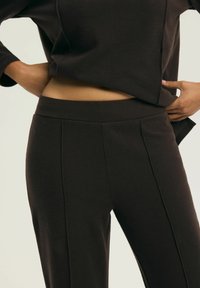 Brązowe, dopasowane spodnie o gładkiej fakturze i szerokim pasie, z pionowymi przeszyciami i średnim stanem.