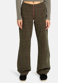 Pantalons à carreaux verts avec une coupe large, fermeture éclair à l'avant et deux grandes poches. Le tissu semble texturé avec une finition douce.
