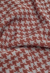 Tissu avec un motif pied-de-poule en rouge brique et gris clair. Le tissu a une texture douce avec des détails de tissage visibles.