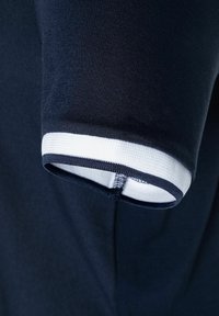 Marineblaue Kleidungsärmel mit einem weiß und marineblau gestreiften Bündchen. Der Stoff erscheint glatt mit einem leichten Glanz und zeigt ein sauberes, modernes Design.