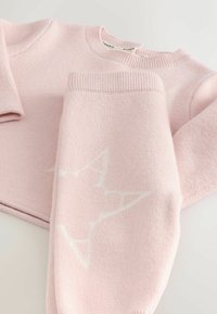 Pletený ružový sveter a nohavice, s bielym hviezdicovým vzorom. Mäkko textúrované s rebrovanými manžetami a výstrihmi.