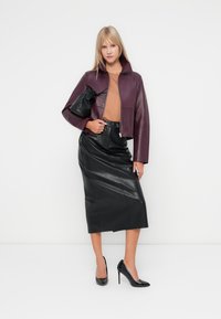 Veste cropped en cuir bordeaux avec un col haut, associée à une jupe crayon en cuir noire et des chaussures à talons hauts noires. Accessoire sac noir.