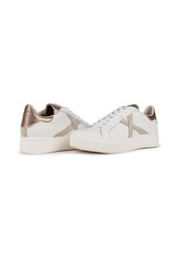 Zapatillas de cuero blanco con acentos texturizados, tacón metálico en rosa dorado, diseño de cordones y suela de goma acolchada. Estilo minimalista.