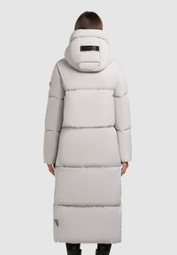 Long, light gray puffer coat with a hood, featuring quilted sections, a black logo patch on the back, and side pockets.