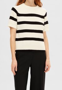 Strikket kortærmet sweater med sorte og hvide vandrette striber, rund halsudskæring samt ribkanter ved nederste kant og ærmer.