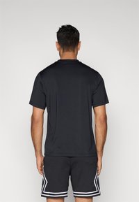 Μαύρο κοντομάνικο t-shirt από λείο ύφασμα, συνδυασμένο με μαύρο σορτς από δίχτυ με λευκές πλαϊνές ρίγες και γεωμετρικά σχέδια.