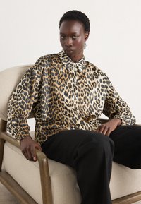 Leopardmønstret skjorte i silke blande, med klassisk krave og knappelukning, lange ærmer og løs pasform. Båret med sorte bukser.