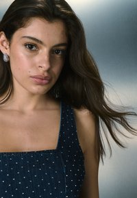 Tume sinine teksakleit, millel on ruudukujuline kaelus ja väikesed kivikesed. Pikkad juuksed voolavad õlgade ümber.