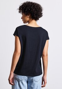 Svart, kortärmad T-shirt med avslappnad passform, rund halsringning och mjukt tyg, i kombination med ljusblå jeans.