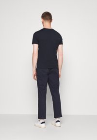 Marinblå t-shirt med kort ärm, ihopparad med mörka byxor och vita sneakers. Enkel design, bomullsmaterial och rund halsringning.