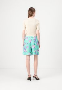 Kremfarget topp med kort erm, kombinert med mintgrønne shorts med blomstermønster. Shortsene har en avslappet passform og en midje med beltehemper.