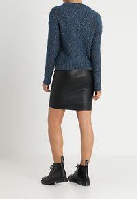 Pull en tricot texturé bleu à col rond, assorti à une mini-jupe en cuir noire et des bottes noires à lacets.