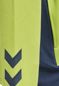 Limegrønne atletiske shorts med en marineblå sidelå, der har tekstureret stof og sorte chevron-designaccenter.