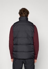 Επενδυμένο μαύρο γιλέκο με ψηλό γιακά, με οριζόντιο ραμμένο σχέδιο, φορεμένο πάνω από ένα μπορντώ πουκάμισο, με απλό λευκό φόντο.