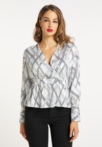 Weiße Bluse mit einem Kettenmuster in Schwarz, mit tiefem V-Ausschnitt, langen Ärmeln und einem Peplum-Taille-Design.