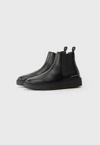 Botas Chelsea de cuero negro con paneles laterales elásticos, acabado suave, punta redondeada y suela de goma plana. Incluyen tiradores para facilitar el calzado.