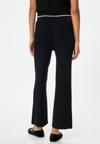 Zwarte geribbelde flared broek met een hoge tailleband en een gestructureerde afwerking, met een split aan de zoom voor extra detail.