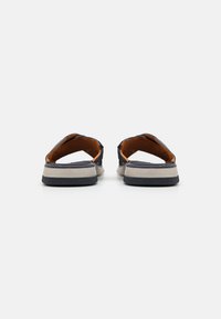 Zwei offene Sandalen in Marineblau mit orangefarbenen Akzenten. Oben aus strukturiertem Stoff und mit einer geschichteten Sohle auf einem grauen Gummiboden.