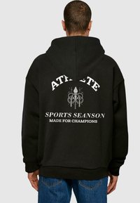 Sudadera con capucha negra con texto blanco en negrita en la parte trasera: "ATLETA", "TEMPORADA DEPORTIVA" y "HECHO PARA CAMPEONES". Diseño de corte casual.