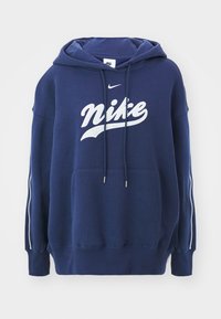 Tmavě modrá mikina s kapucí vyrobená z měkké látky, s přední kapsou, bílým logem Nike, kapucí se stahovací šňůrkou a kontrastními bílými pruhy na rukávech.