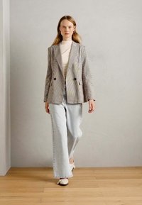 Hellgrau karierter Blazer im Double-Breasted-Design, kombiniert mit hellblauen weiten Jeans und weißen Schuhen. Glatte Textur, dezentes Muster.