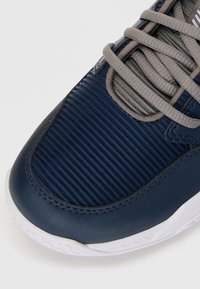 Marineblå sneaker med en glat lædertås, tekstureret stofoverdel og grå snørebånd. Hvid gummisål med mønstret slids.