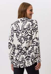Silk blouse featuring a bold black and white abstract floral pattern, long sleeves, a collar, and buttoned cuffs, viewed from the back.