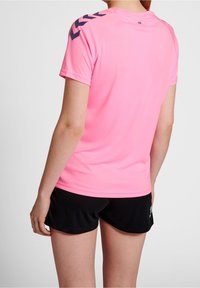 Różowa koszulka sportowa z krótkimi rękawami, z ciemnoniebieskimi akcentami w kształcie zygzaków na ramionach. Gładka struktura, lekki materiał, praktyczny design.