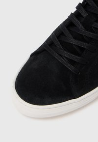 Adidașii din suede negru au vârful rotund, un exterior texturat și șireturi plate negre. Talpa exterioară din cauciuc alb are detalii discrete de cusătură.