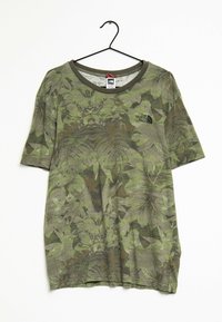 Camiseta de camuflaje verde con mangas cortas, con un patrón de hojas, cuello redondo y un pequeño logo negro en el pecho.