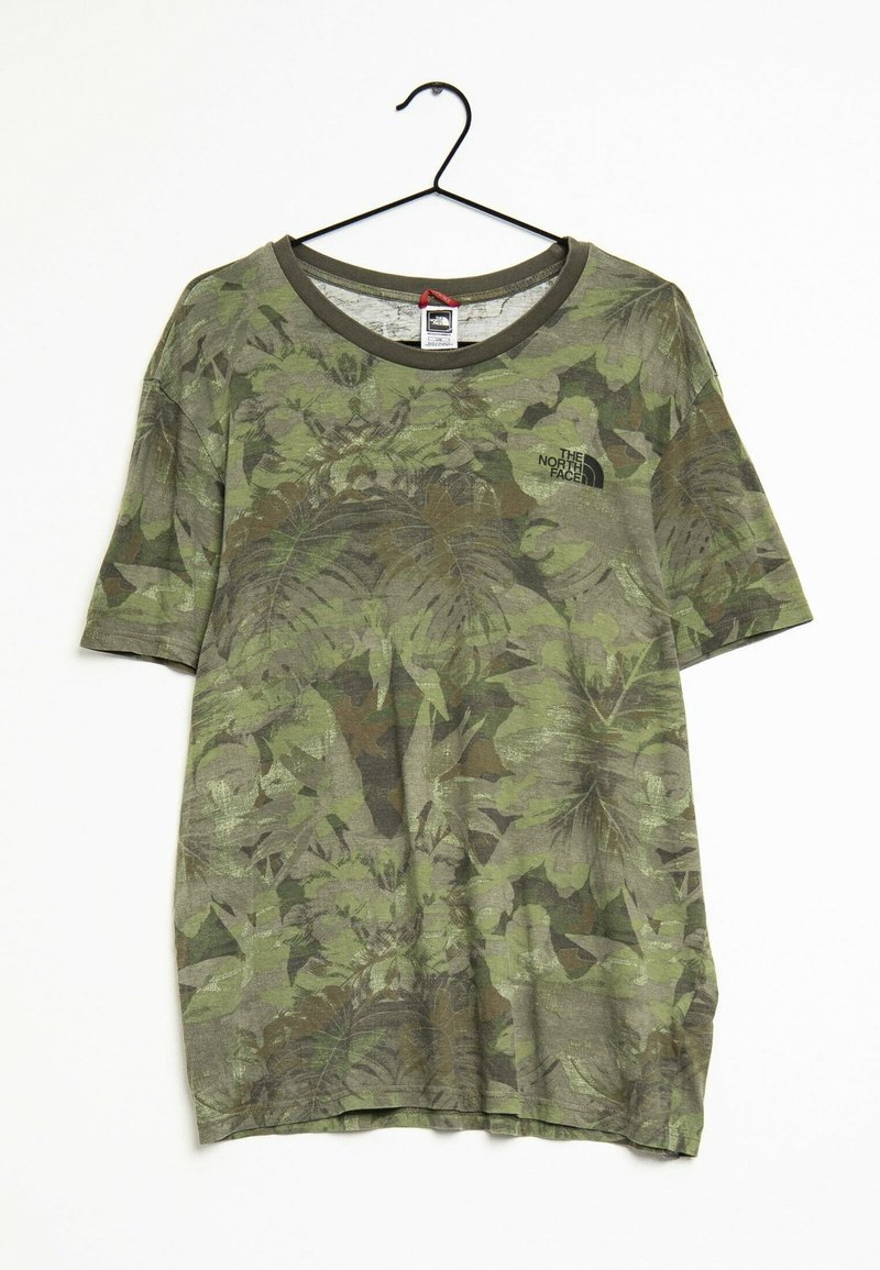 Camiseta de camuflaje verde con mangas cortas, con un patrón de hojas, cuello redondo y un pequeño logo negro en el pecho.