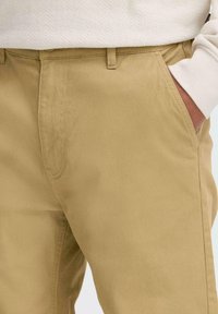 Beige chinos made of cotton, featuring a smooth texture, angled side pockets, and a straight-leg design with a waistband.