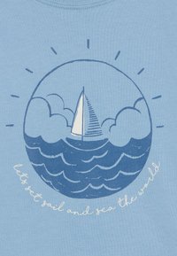 Maglietta azzurro chiaro con un design nautico: una vela bianca su onde blu, circondata da nuvole e raggi di sole, con testo: "salpiamo e vediamo il mondo."