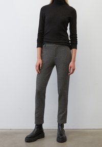 Un haut noir à col montant associé à un pantalon gris à motifs, arborant une coupe ajustée et une conception longueur cheville, complété par des bottes massives noires.