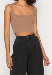 Top corto marrón de canalé con escote cuadrado ancho, combinado con pantalones sueltos negros de tiro alto. Botón con logo visible en los pantalones.