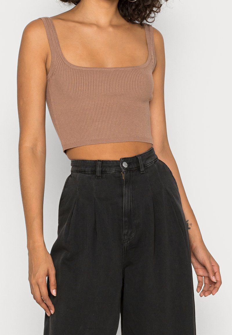 Top corto marrón de canalé con escote cuadrado ancho, combinado con pantalones sueltos negros de tiro alto. Botón con logo visible en los pantalones.