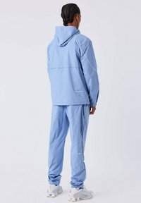 Lichtblauwe trainingsjack met capuchon en bijpassende broek; heeft witte accenten en een losse pasvorm. Gemaakt van een glad, lichtgewicht materiaal.