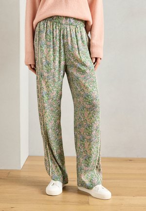 Lillelille mustritega rohelised püksid, millel on elastne vöökoht ja külgmised triibud, valmistatud kergest materjalist, koos valgete tossudega.