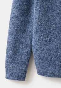Gros plan d'une manche de pull en laine bleue tricotée montrant un tissu doux et texturé avec un détail de bord-côte.