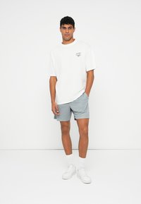 Hvid bomulds t-shirt med rund halsudskæring og lille grafik, parret med lyseblå shorts og hvide sneakers med hvide sokker.