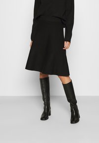 Svart trumpetkjol med en slät textur, hög midja och knä-lång fåll. Kombineras med eleganta svarta knähöga stövlar.