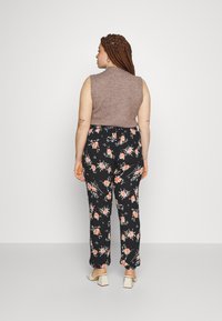 Un top fără mâneci de culoare maro, asortat cu pantaloni negri cu flori, având un model vibrant de trandafiri. Ținuta este completată cu o pereche de pantofi cu toc bloc de culoare crem.
