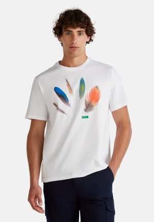 Camiseta de algodón blanca con estampados de plumas coloridas en azul, verde, naranja y marrón. Incluye una pequeña etiqueta verde cerca del dobladillo.