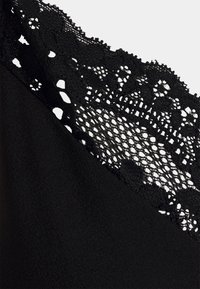 Czarny top z materiału z koronkowymi detalami przy dekolcie, prezentujący misternie wzory i miękkie, teksturowane wykończenie.