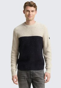 Strickpullover mit cremefarbenen und marineblauen horizontalen Farbbl�öcken, gerippter Textur, Rundhalsausschnitt und gesprenkelten Details. Kombiniert mit grauen Jeans.