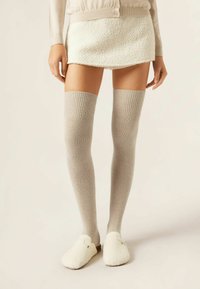 Knæhøje ribbede sokker i lys grå, lavet af blødt strikmateriale, sat sammen med en struktureret hvid mini-sko og fluffy hvide slippers.