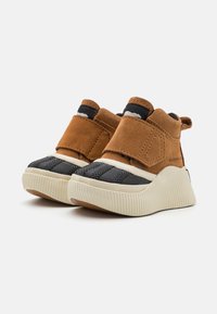 Bruna mocka ankelstövlar med kardborreband, svarta nätdetaljer och en tjock, räfflad vit sula. Texturerad design med gummibotten.