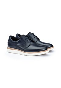 Chaussures en cuir marine avec une finition lisse, dotées d'une semelle blanche et d'un accent beige. Conception à lacets avec un bout arrondi et un style minimal.